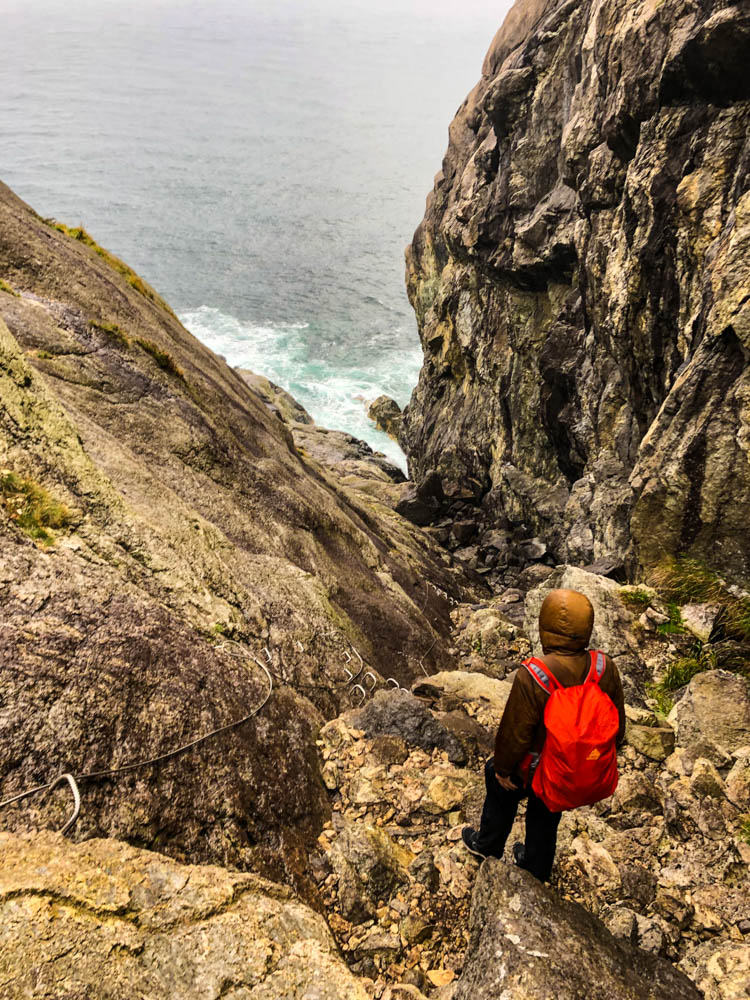 Julian steht auf einem Felsvorsprung und schaut auf den Atlantik. Vor im liegt die Rinne zu den Brufjell Höhlen.