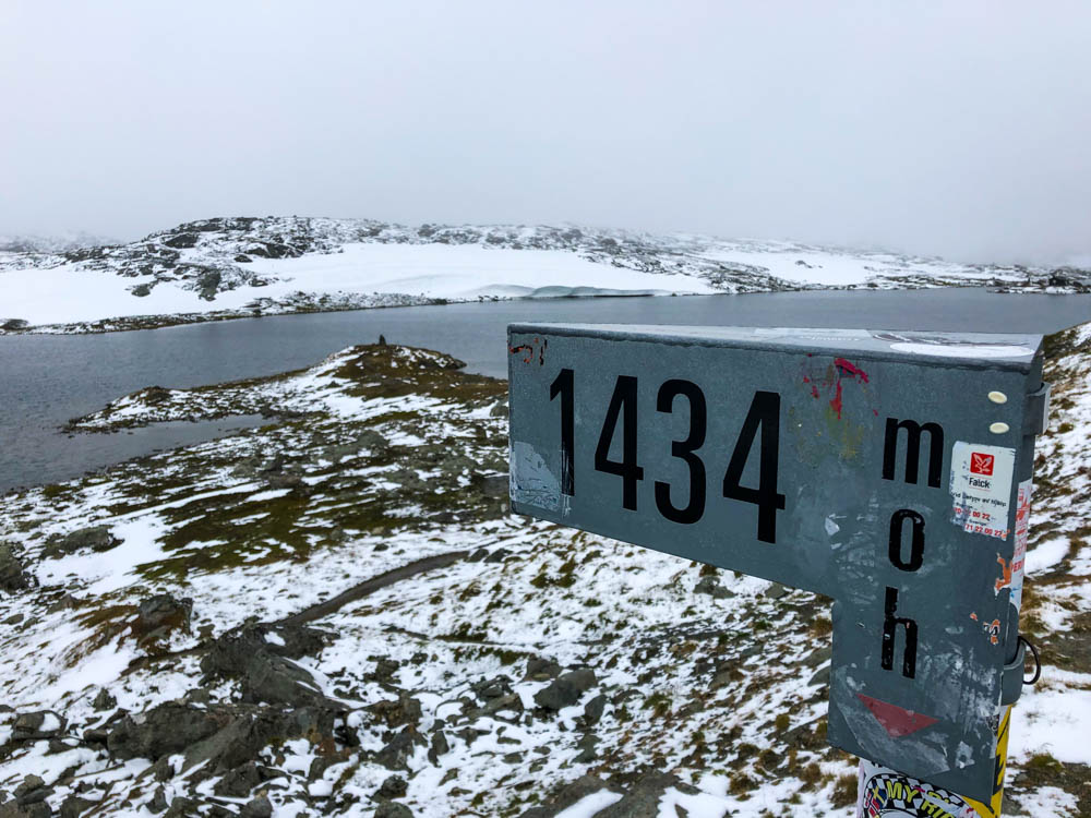 Die Höhenangabe von 1434m auf einem Schild am höchsten Punkt des Passes. Im Hintergrund liegt Schnee.