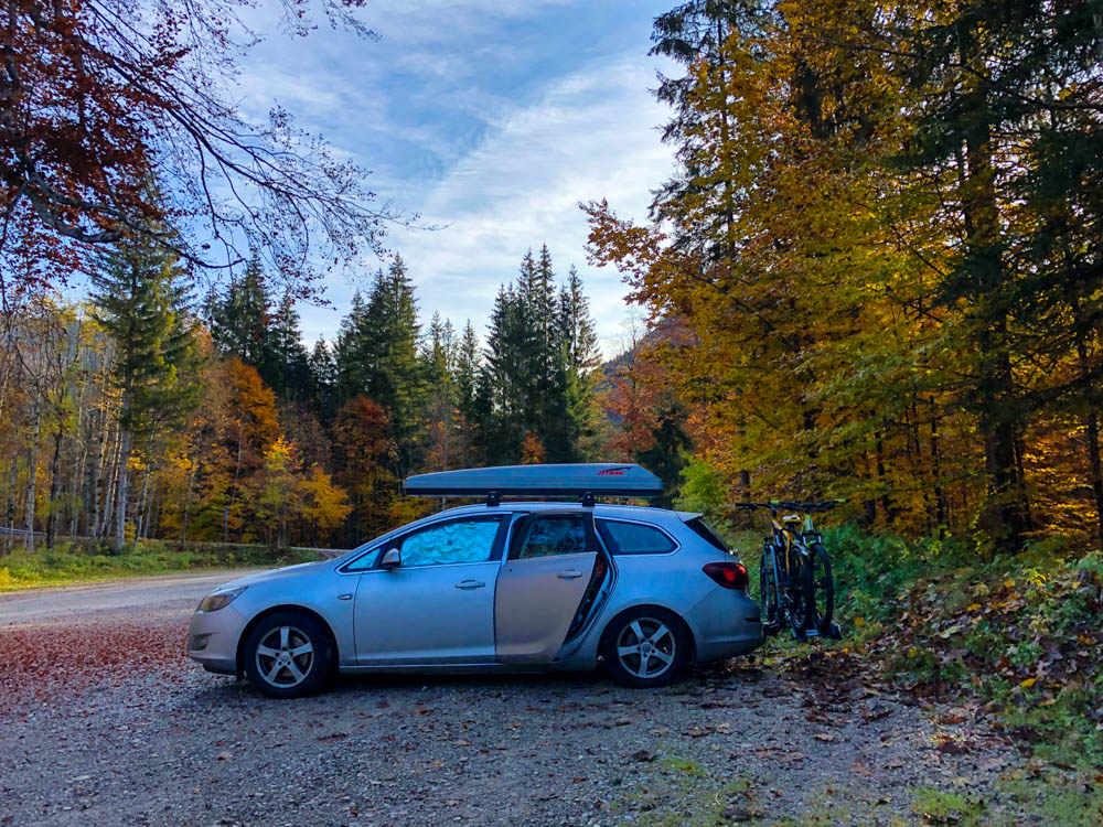 Deutsche Alpen - Blick auf Microcamper. Auto steht auf Waldparkplatz und die Umgebung sieht herbstlich aus.