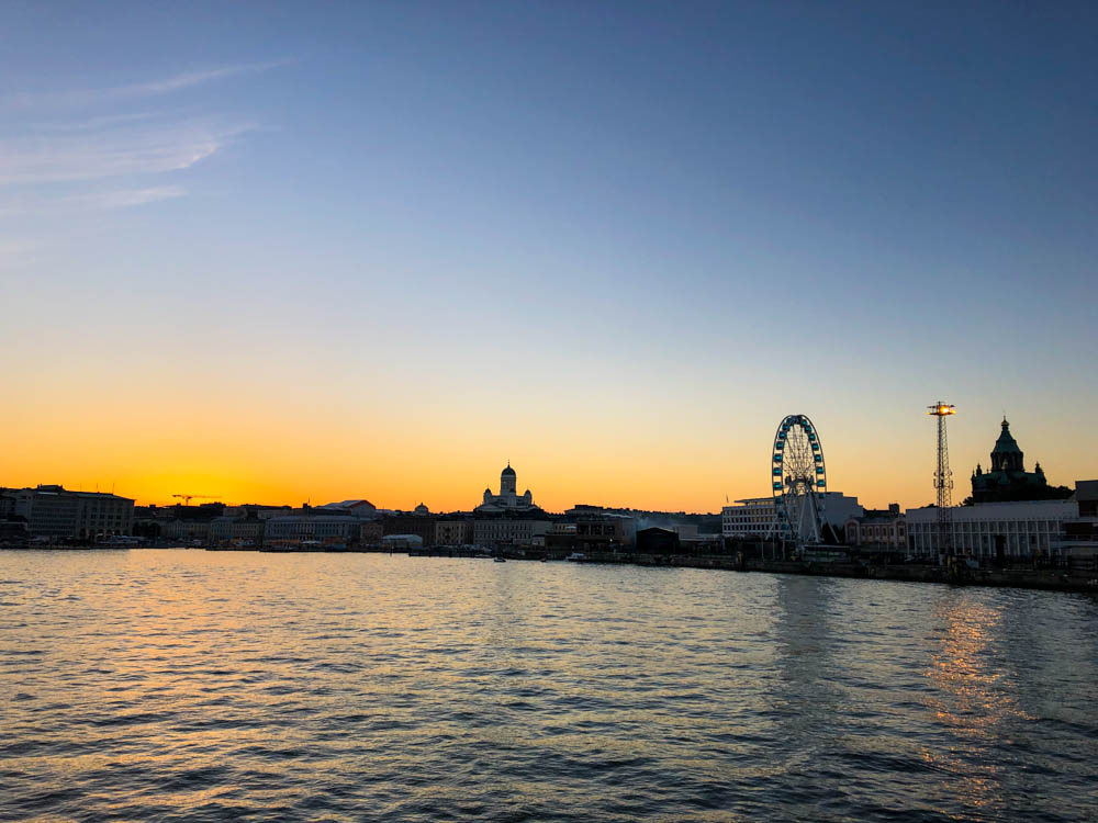 Sonnenuntergang über Helsinki. Es ist nur die Silhouette der Skyline zu erkennen. Man sieht deutlich den Dom, das Riesenrad und die Uspenski-Kathedrale.