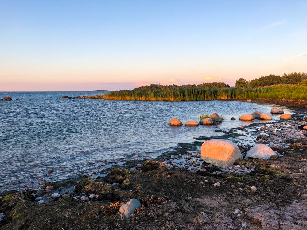 Strand mit Felsen in Käsmu. Die Sonne beginnt unter zu gehen und der Himmel färbt sich bereits leicht orange. Über den Norden Estlands in die Hauptstadt