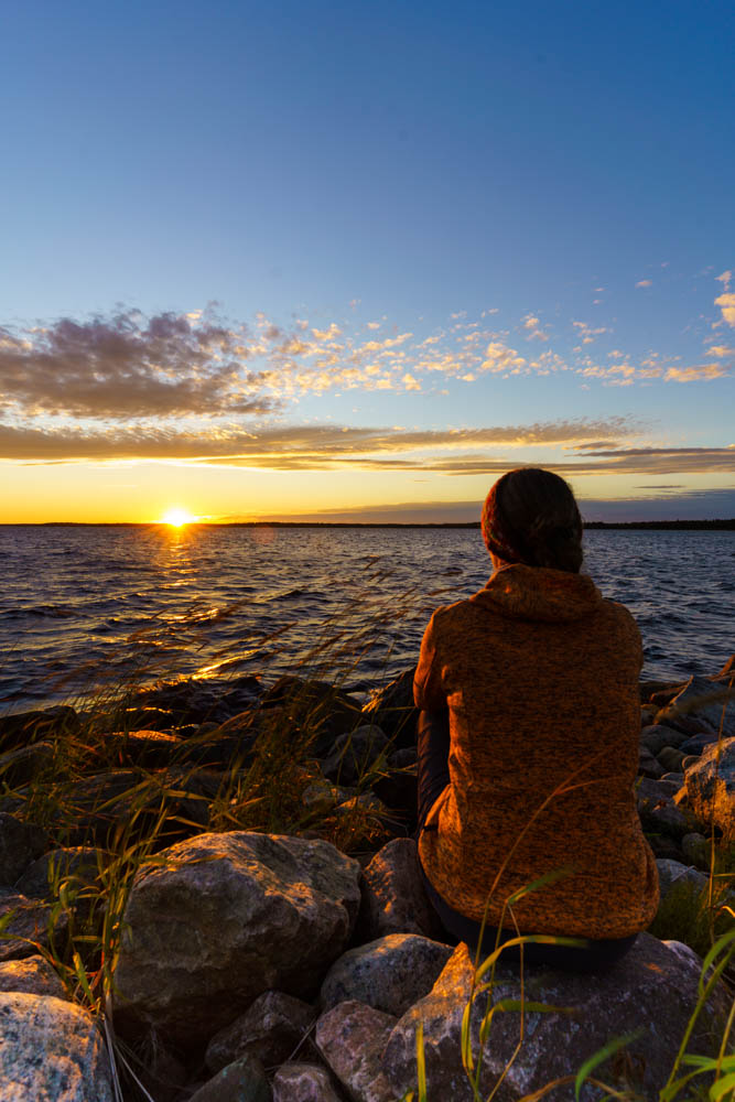 Melanie sitzt am Meer und betrachtet den Sonnenuntergang über der finnischen Ostsee. Goodbye Ostsee - auf nach Lappland