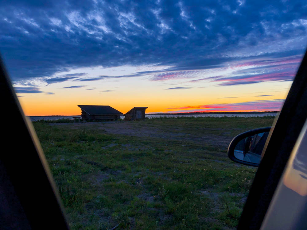 Blick aus unserem Auto/Camper in Richtung finnischer Ostsee. Im Bild sind zwei Hütten zu sehen und dahinter Sonnenuntergang in allen Farben. Goodbye Ostsee - auf nach Lappland