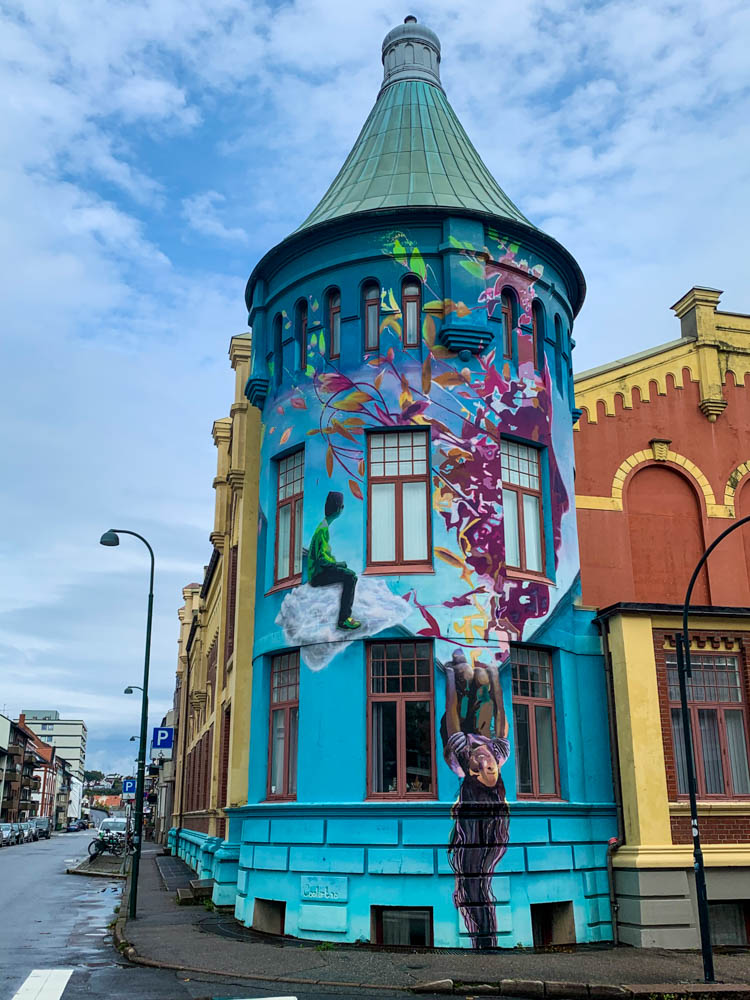 Street Art in Kristiansand. Auf einem Turm ist ein buntes Graffiti mit zwei Kindern zu sehen. Tour bis nach Kristiansand