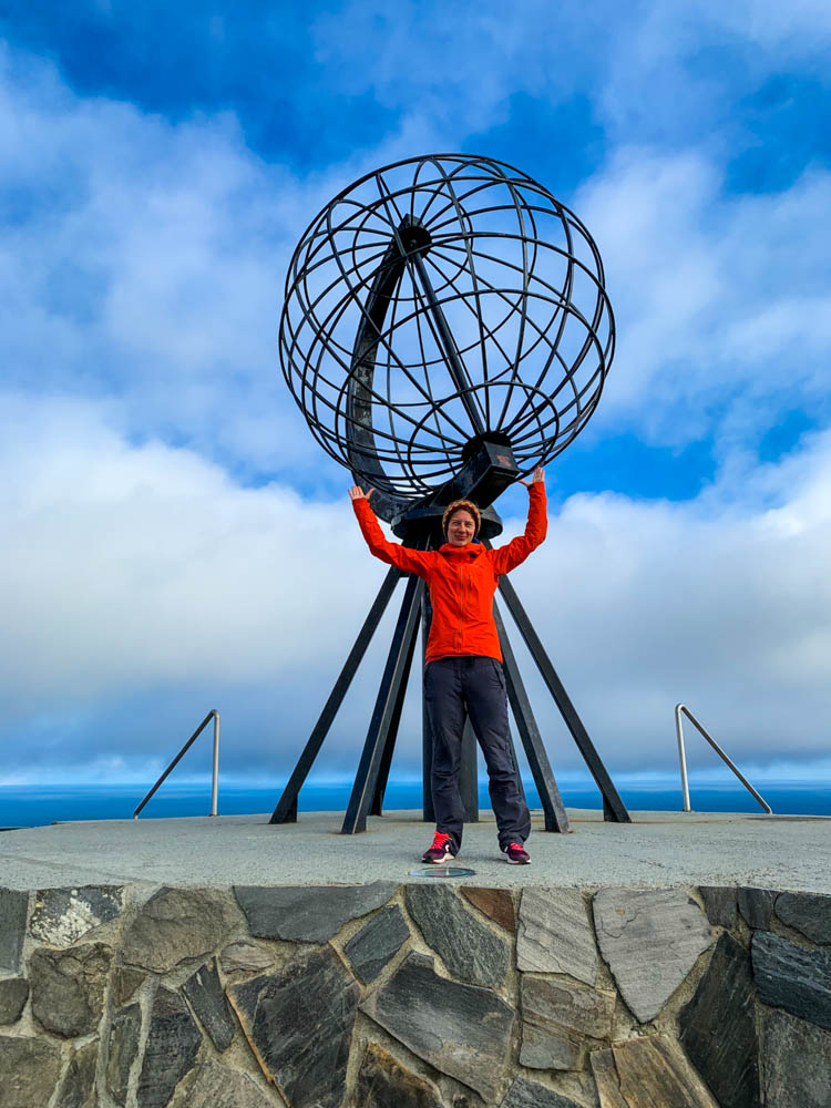 Melanie steht vor dem Globus am Nordkapp und es sieht so aus, als würde sie den Globus über sich stemmen. Fjorde, Berge und Seen, Norwegen
