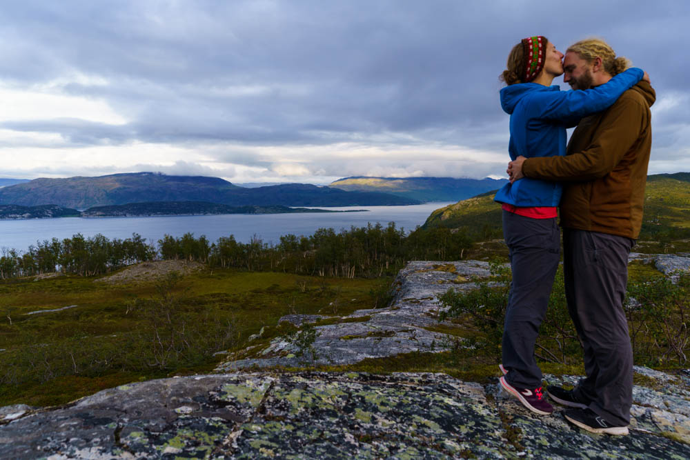 Melanie und Julian posieren stehend vor wilder Landschaft Norwegens. Alta bis zu den Lofoten