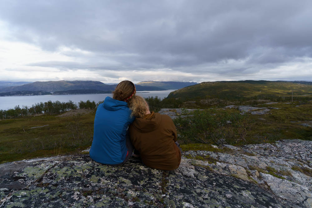 Melanie und Julian posieren sitzend vor wilder Landschaft Norwegens. Alta bis zu den Lofoten