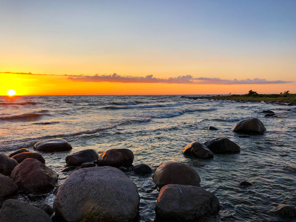 Die Wellen der Ostsee umspülen Steine im Wasser vor Purekkari. Die Sonne geht gerade am Horizont unter uns versinkt im Meer.