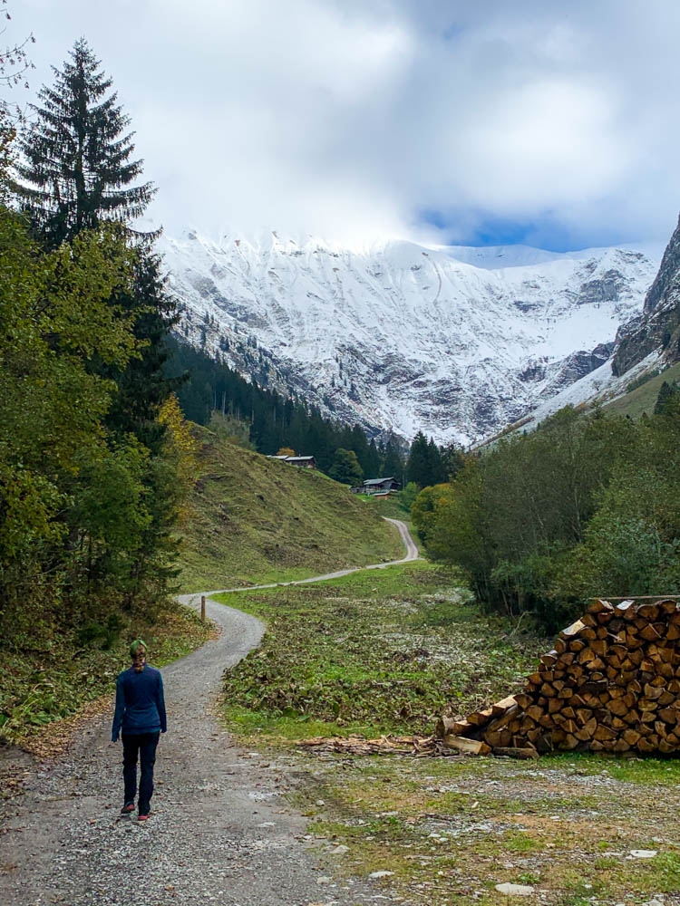 Melanie läuft auf der Fahrstraße Richtung Hintere Traufberg Alpe. Im Hintergrund sind die Alpe und schneebedeckte Berge zu sehen. Tour durch die deutschen Alpen