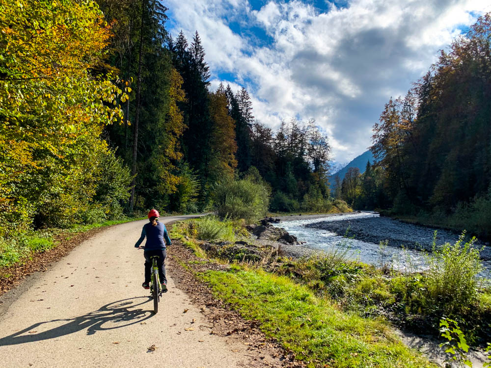 Melanie fährt mit dem Fahrrad durch Trettachtal. Die Sonne scheint und die Blätter sind leicht herbstlich verfärbt. Tour durch die deutschen Alpen