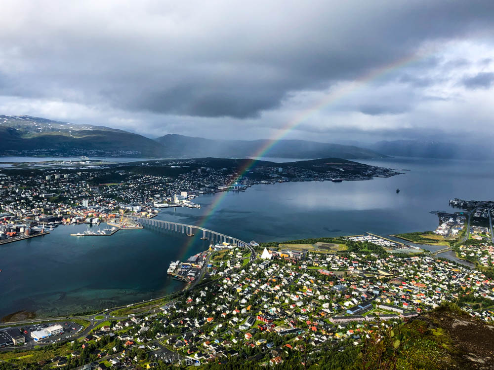 Blick auf Tromsø vom Hausberg Storsteinen. Über der Stadt hat sich ein regenbogen gebildet. Die Wolken sind düster und es sieht nach Unwetter aus.