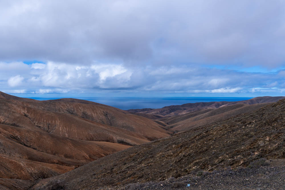 Hügellandschaft Fuerteventura, am Horizont ist der Atlantik zu sehen und einige Wolken.