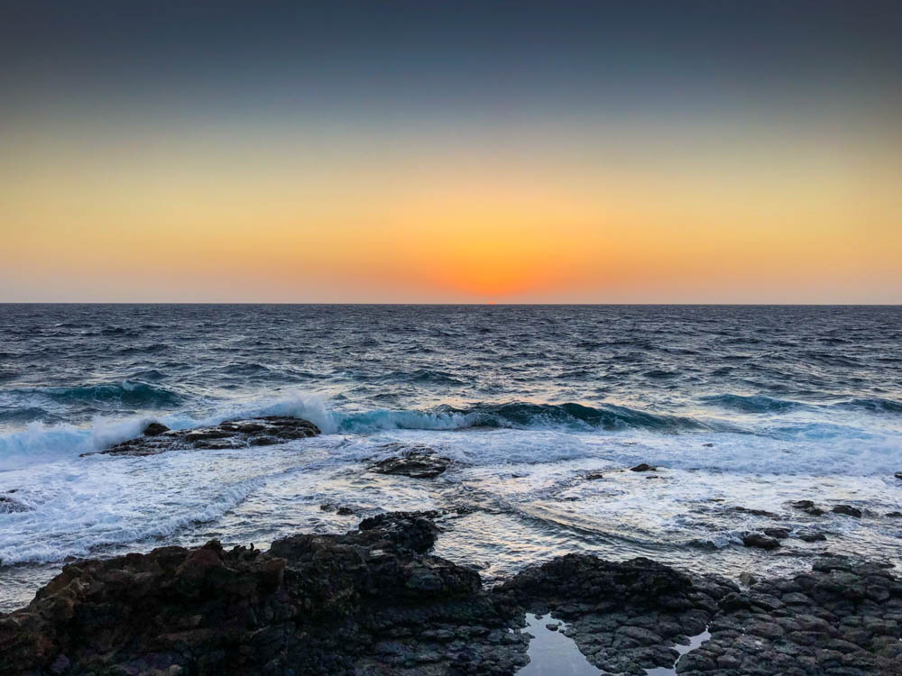 Sonnenaufgang über dem Atlantik. Der Himmel brennt orange während unten die Wellen gegen den Fels branden.