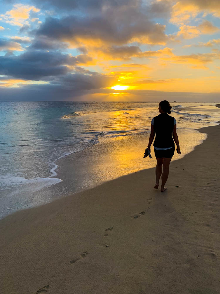 Melanie läuft entlang des Strandes in Jandia. Im Hintergrund geht die Sonne unter und der Himmel brennt orange. Erkundungstouren auf Fuerteventura