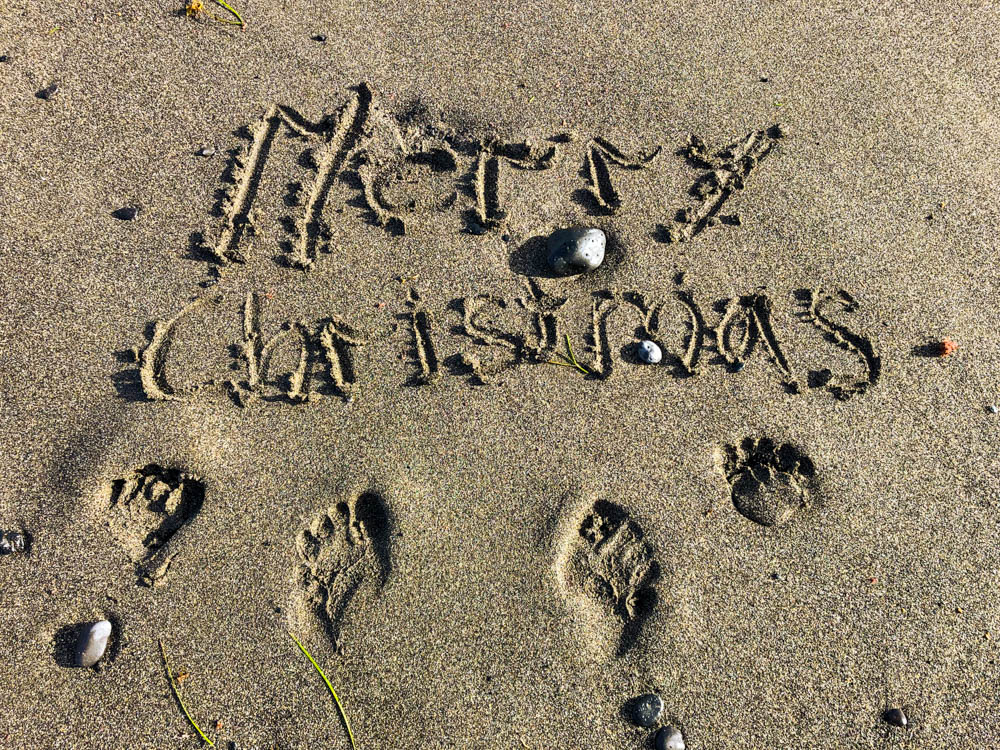 In den Sand am Strand sind die Worte "Merry Christmas" geschrieben, zudem sind die Fußabdrücke von Melanie und Julian zu sehen. Weihnachten unter Palmen