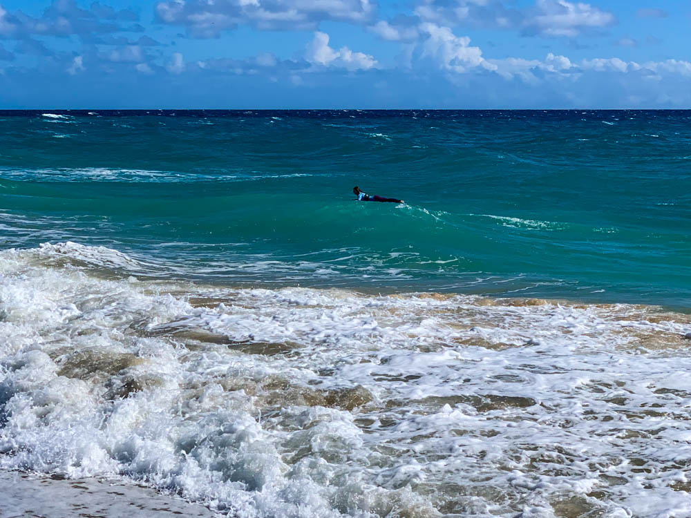 Melanie liegt auf ihrem Surfbrett und paddelt durch die hohen Wellen und die starke Strömung. Wassersport im Süden von Fuerteventura