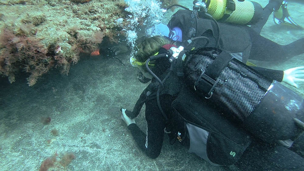 Melanie und Bernd liegen am Meeresgrund und schauen unter einer Felsspalte nach einem Meeresbewohner. Bernd leuchtet mit einer Tauchlampe in die Spalte. Wassersport im Süden von Fuerteventura