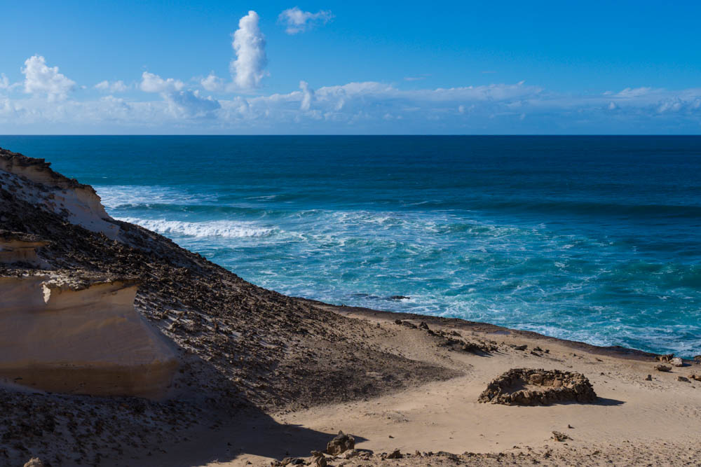 Die Wellen vom Atlantik rollen Richtung sandiger Westküste. Links ist ein Berg aus Sand und Lavastein zu sehen.