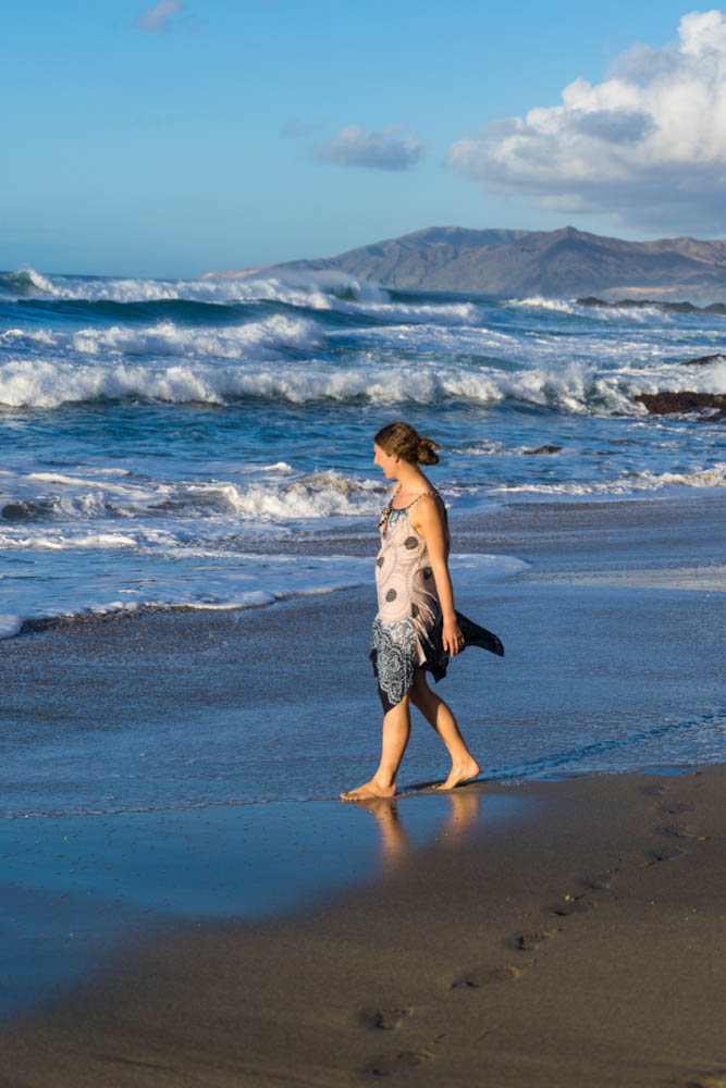 Melanie läuft am Strand der Westküste entlang. Die Wellen im Hintergrund sind hoch und haben alle eine weiße Schaumkrone.