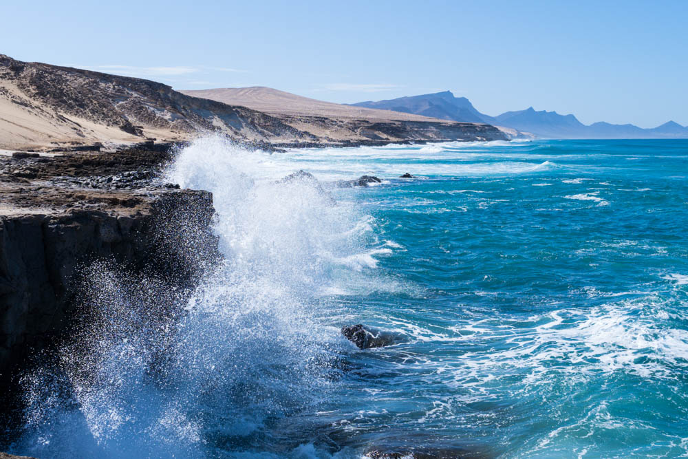 Die Wellen schlagen an die Felsen der Westküste und die Gischt spritzt stark nach oben.