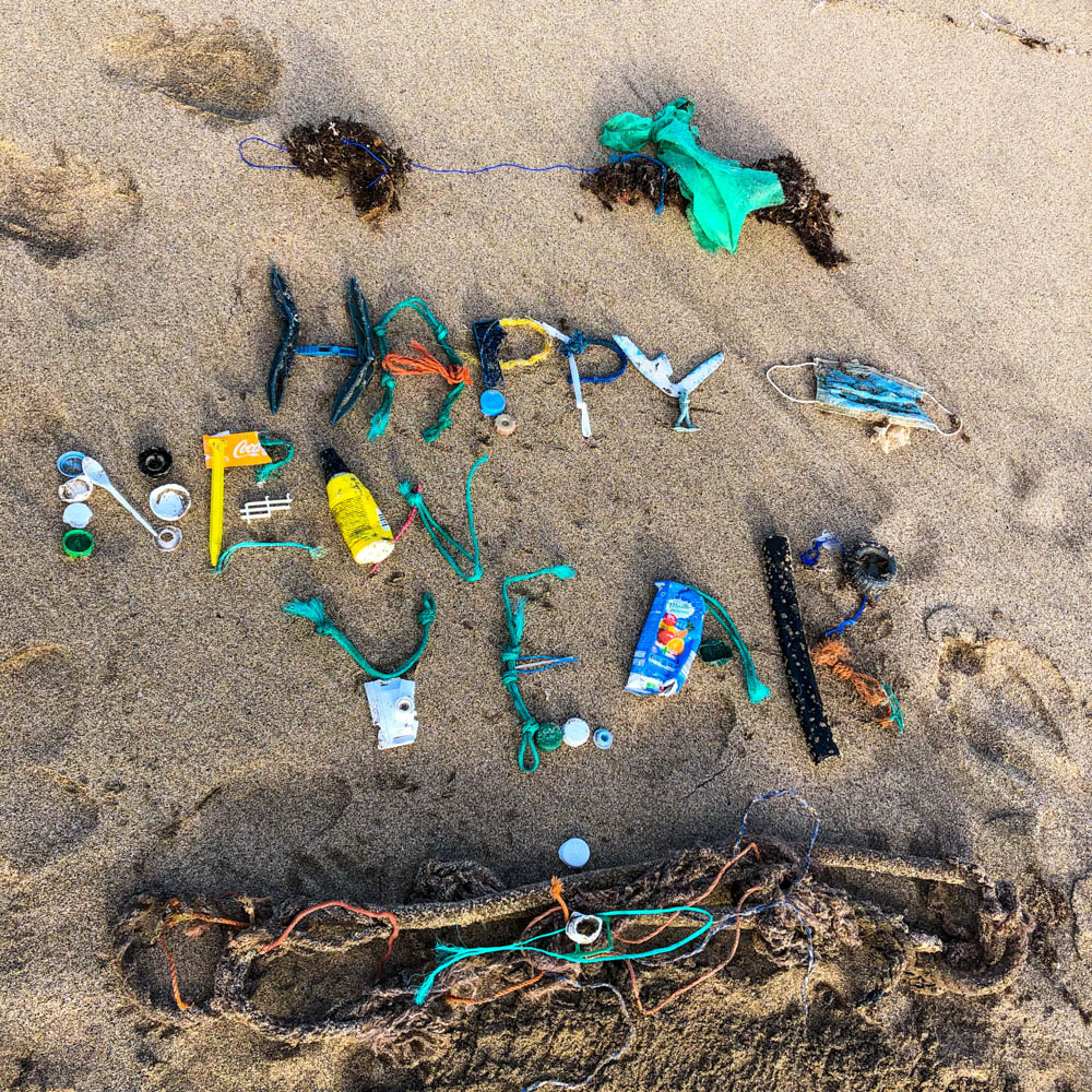 Mit Plastikmüll wurde Happy New Year in den Sand "geschrieben". Frohes Neues - Happy New Year - Feliz Año Nuevo