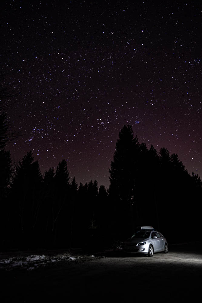 Frontaufnahme von Astrarix unter einem gigantischen Sternenhimmel. Das Auto wird von einer Taschenlampe seitlich angeleuchtet. Erste Nacht zurück in Deutschland im Camper.