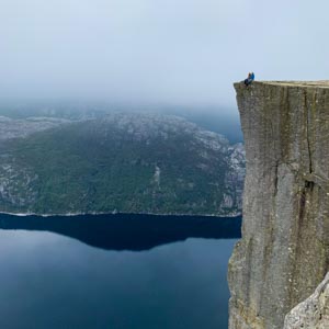 Norwegens Süden - Rund um den Preikestolen. Melanie und Julian sitzen auf der Spitze des Preikestolen und lassen die Füße über den Abgrund baumeln.