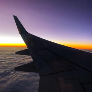 Blick aus Flugzeugfenster auf Flügel des Flugzeugs. Die Sonne ist untergegangen und der Horizont ist orange verfärbt. Zeit in Fuerteventura