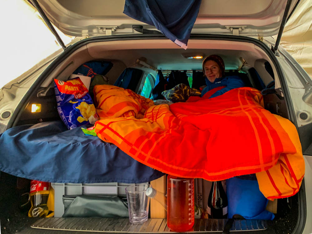 Melanie liegt im Mini-Camper Astrarix, das Autozelt ist um den Kofferraum gespannt.