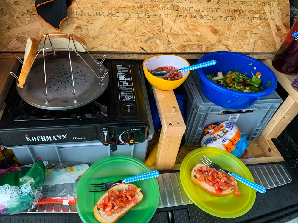 Nahaufnahme Küche Mini-Camper Astrarix. Es wird gerade Brot getoastet, dazu gibt es Salat und Bruschetta.