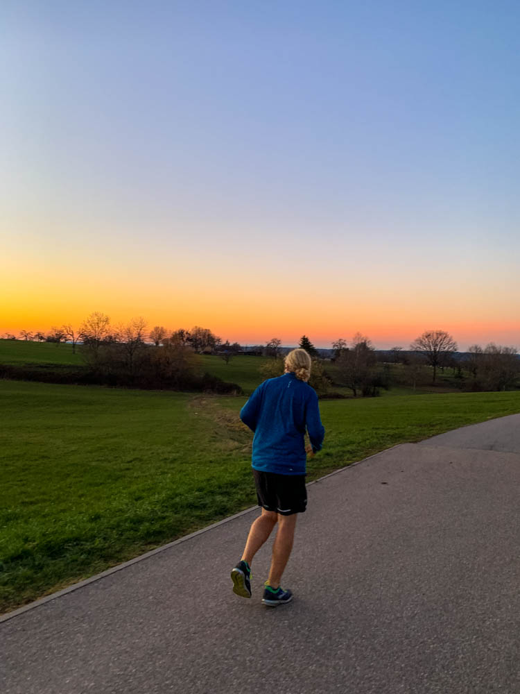 Julian joggt in den Sonnenuntergang. Im Hintergrund sind Obstwiesen zu sehen und der Himmel brennt in den Farben gelb, orange und rot.