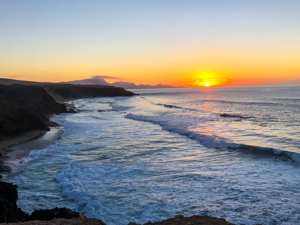 Sonnenuntergang an der Küste von La Pared. Die Sonne versinkt gerade stimmungsvoll im Meer und zaubert die tollsten rot, orange und gelb Töne an den Himmel. Es rollen große Wellen an die Westküste vor Fuerteventura.
