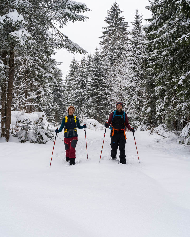 Melanie und Julian laufen mit ihren Schneeschuhen durch den tiefen Schnee und schauen dabei in die Kamera. Der Weg vor ihnen ist unverspurt und es gibt eine schöne Schneedecke..