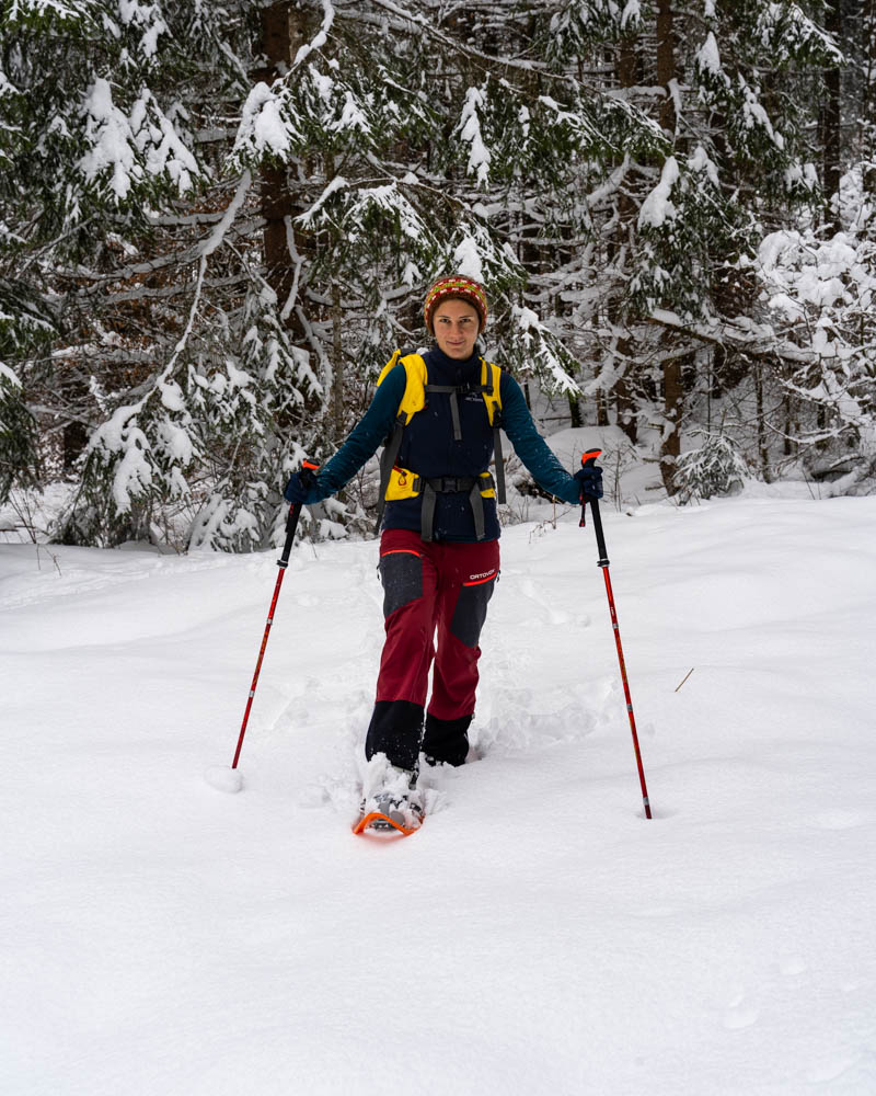 Melanie stapft mit ihen Schneschuhe durch die unberührte Winterlandschaft und lächelt in die Kamera.