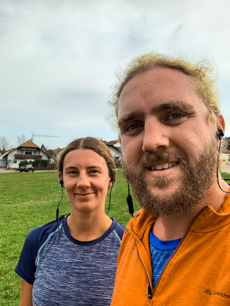Selfie von Melanie und Julian nach dem Joggen (erstes mal joggen zurück in Deutschland). Beide tragen Ohrhörer und lächeln in die Kamera.
