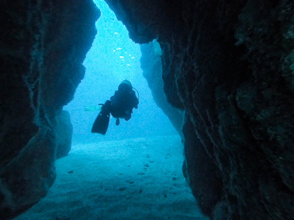 Melanie schwimmt durch einen Durchgang zwischen einer Felsformation am Meeresgrund. Diese Stelle nennt sich El Portal - Abtauchen auf Fuerteventura