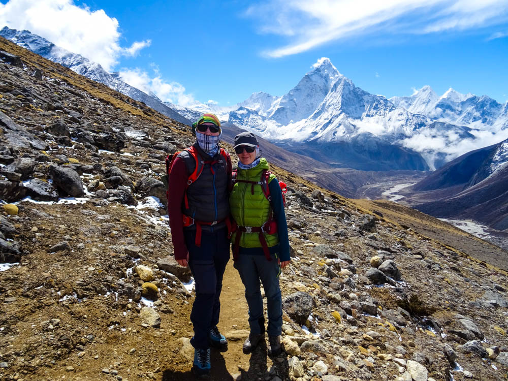 Melanie und Julian stehen vor einer schönen Bergkulisse im Himalaya Gebirge, der Ama Dablam sticht hinter ihnen heraus. Fortsetzung Trekking Mount Everest Region. Reise Blog