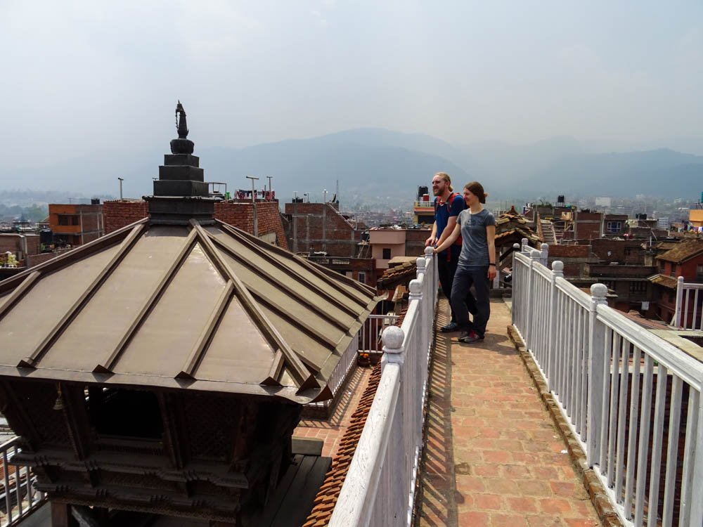 Melanie und Julian stehen auf einer Dachterrasse in Bhaktapur und schauen die Dächer der Stadt. Im Hintergrund sind viele Häuser zu sehen. Fernreise Nepal Eindrücke