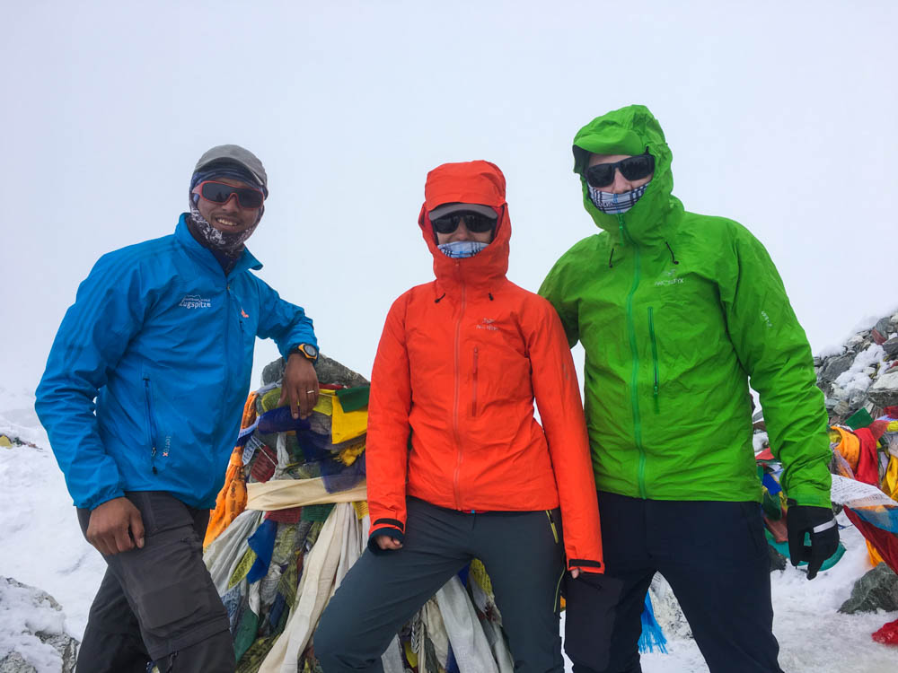 Melanie, Julian und Guide Keshar stehen am höchsten Punkt des Cho La Pass und grinsen in die Kamera. Der Himmel rund herum ist komplett weiß vom Nebel. Fortsetzung Trekking Mount Everest Region