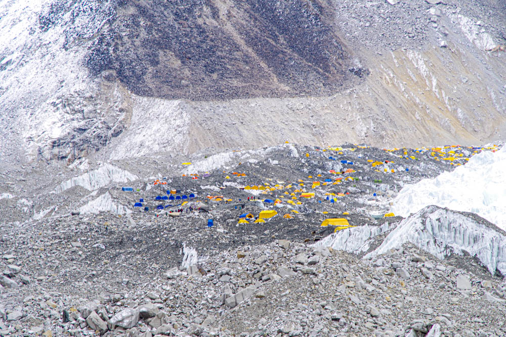 Mount Everest Base Camp mit der Kamera herein gezoomt. Es sind bunte Zelte in einem ansonsten weißen Bild zu sehen. Khumbu-Gletscher und Schnee- und Gerölllandschaft Trekking Fortsetzung