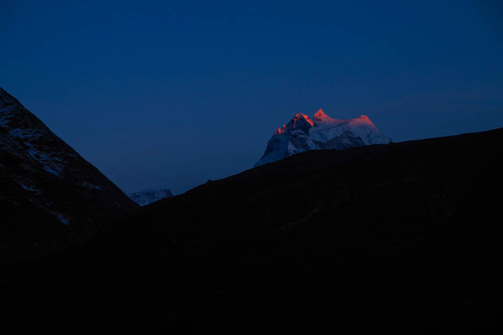 Abendaufnahme von einem Bergmassiv bei Trekking in Nepal zu Mount Everest Base Camp. Die Sonne geht gerade unter und die Spitzen der Gipfel sind rot beleuchtet.