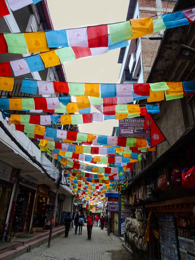 Typische Straße im Touristenviertel Thamel in Kathmandu. Es hängen über der kompletten Straße etliche bunte Gebetsfahnen. Eindrücke einer Fernreise nach Nepal. Ausflugstipps in und um Kathmandu