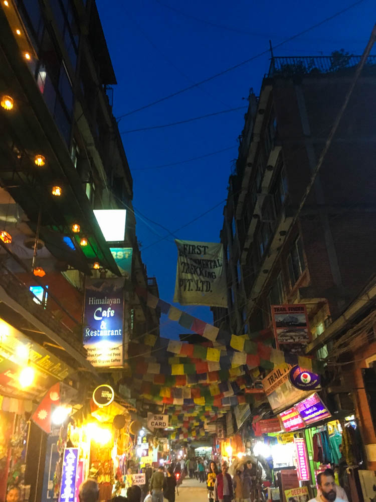 Touristenviertel Thamel in Kathmandu bei Nacht. Es ist eine Fußgängerzone zu sehen, über den Straßen hängen bunte Gebetsfahnen.