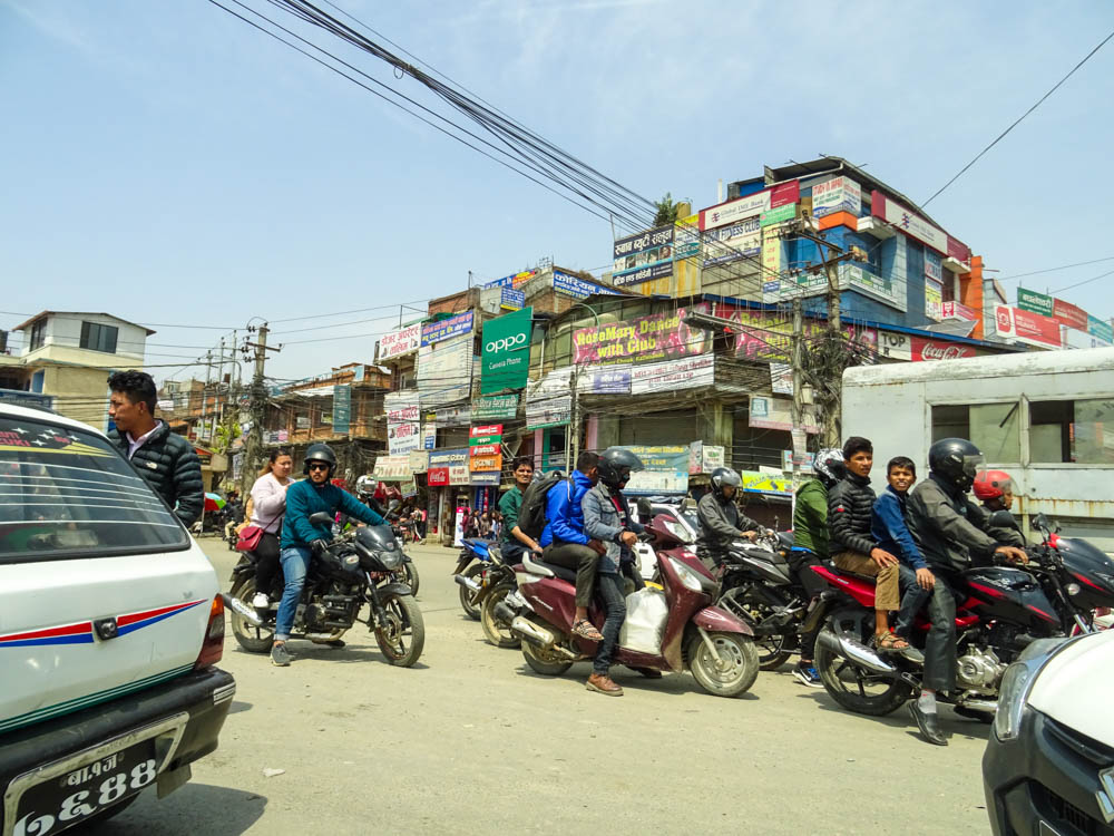 Typisches Straßenbild von Kathmandu bei Fernreise Nepal. Es sind mehrere Roller unterwegs, auf denen teilweise mehr als 2 Personen sitzen. Nur die Fahrer tragen Helme.