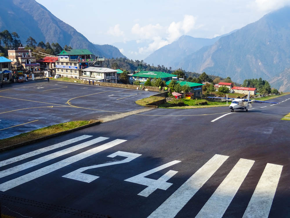 Aufnahme vom Flughafen in Lukla (Nepal). Es rollt gerade eine gelandete Maschine auf der steilen Landebahn Richtung Flughafen Vorplatz.