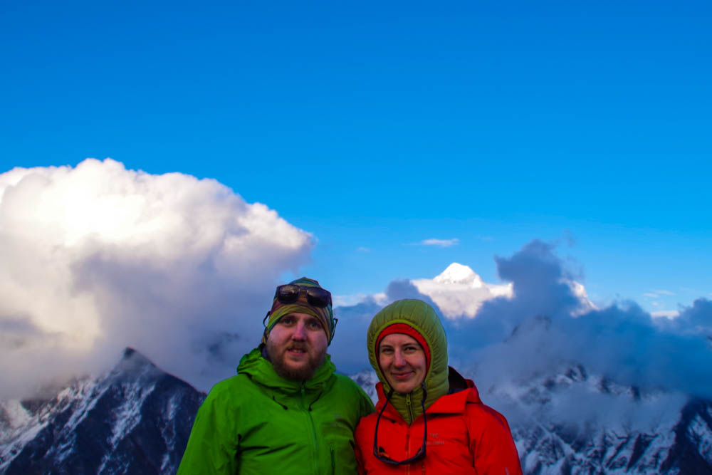 Melanie und Julian stehen auf dem Gokyo Ri und hinter ihnen ist die Spitze des Mount Everest zu sehen. Der Himmel ist blau und es sind ein paar wenige Wolken zu sehen. Trekking Mount Everest Base Camp