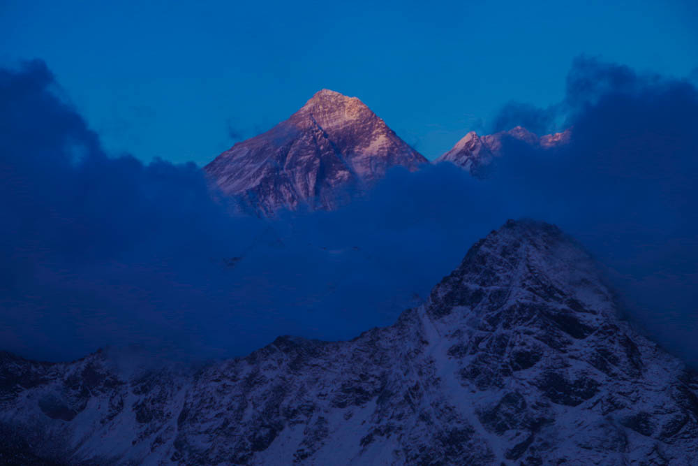 Die Spitze des Mount Everest ist rot gefärbt. Es hängen ein paar Wolken vor den Bergen. Trekking Mount Everest Base Camp