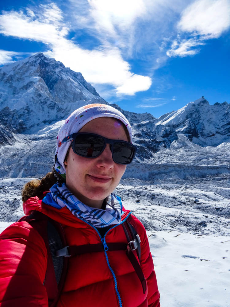 Selfie von Melanie auf dem Weg zum Mount Everest Base Camp. Melanie sticht mit ihrer roten Jacke aus dem sonst weißen Bild heraus. Die Berge sind schneebedeckt und es liegt überall Schnee, der Himmel ist blau. Trekking Fortsetzung
