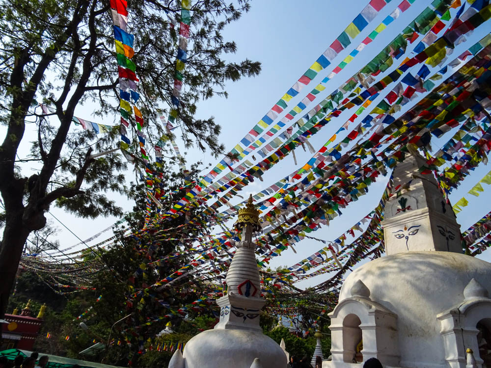 Bunte Gebetsfahnen über Tempelanlage Swayambhunath - Fernreise Nepal. Im rechten Teil des Bildes sind zudem zwei Stupa zu sehen.
