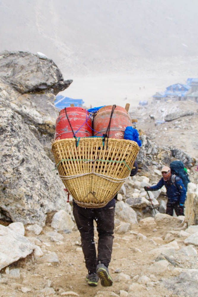 Ein Träger hat in einem Korb zwei große Gasflaschen. Träger in Nepal